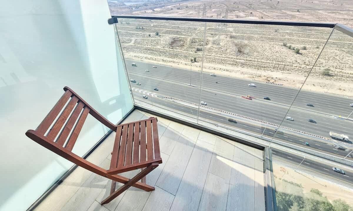 Een balkon met een houten stoel en uitzicht op een snelweg.