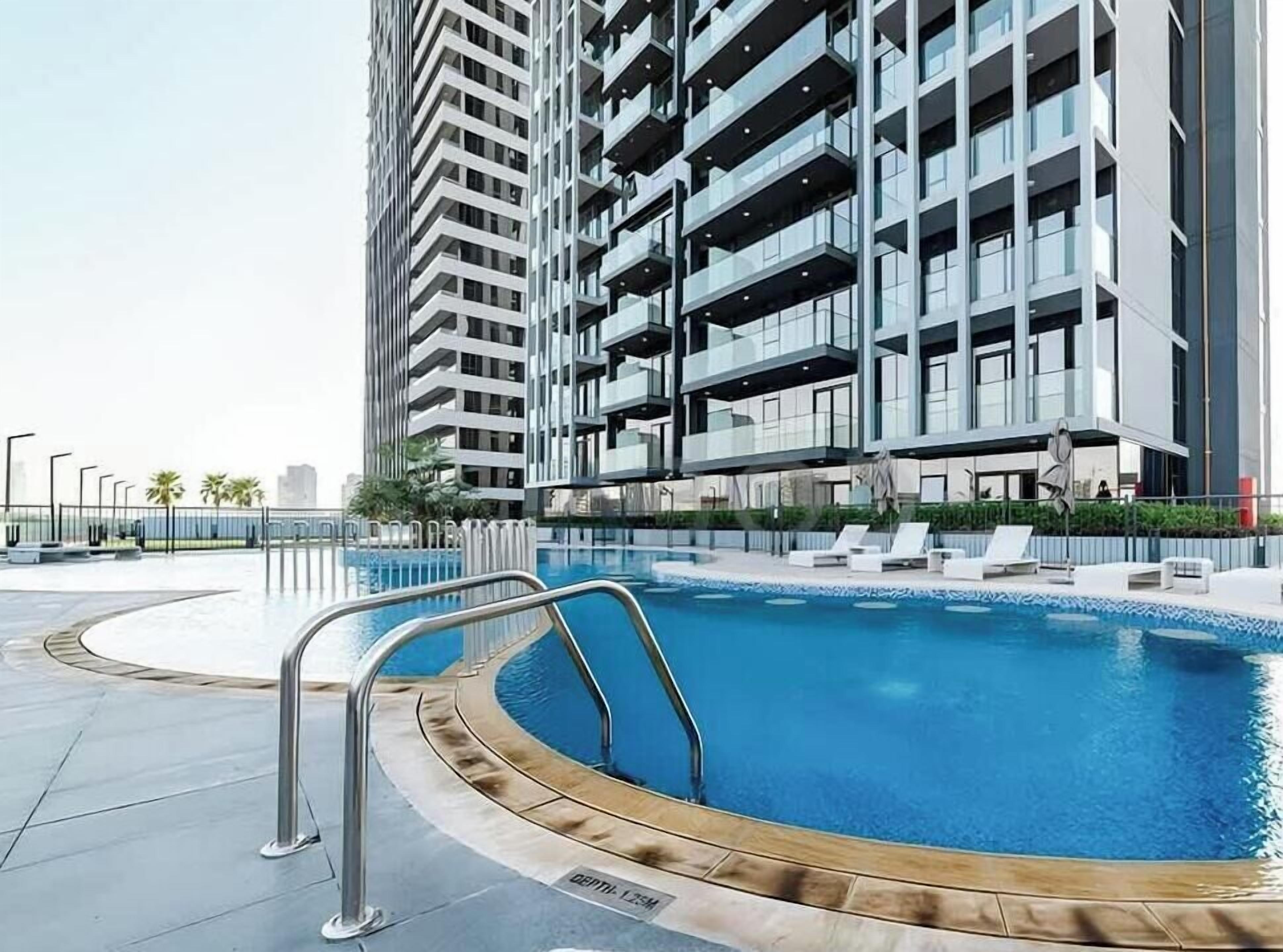 A modern building with a swimming pool, balconies, and a clear sky.