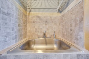Un baño con lavamanos de acero inoxidable, azulejos color beige y una lámpara en el techo.