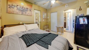 Een slaapkamer met een bed, een plafondventilator, een koelkast en een schilderij van zebra's.