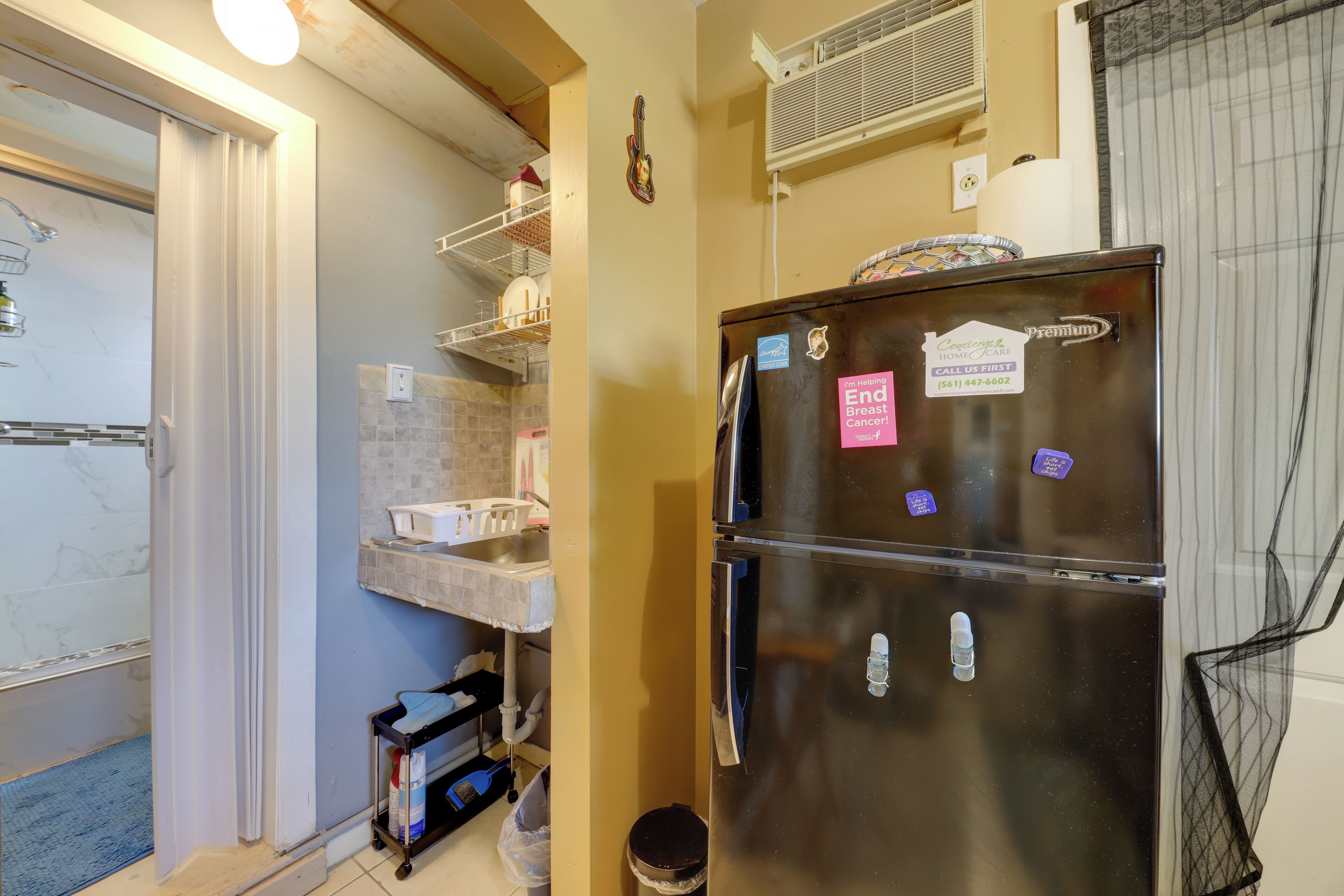 A compact kitchen with a double-door refrigerator, a built-in sink, and a small trash bin.