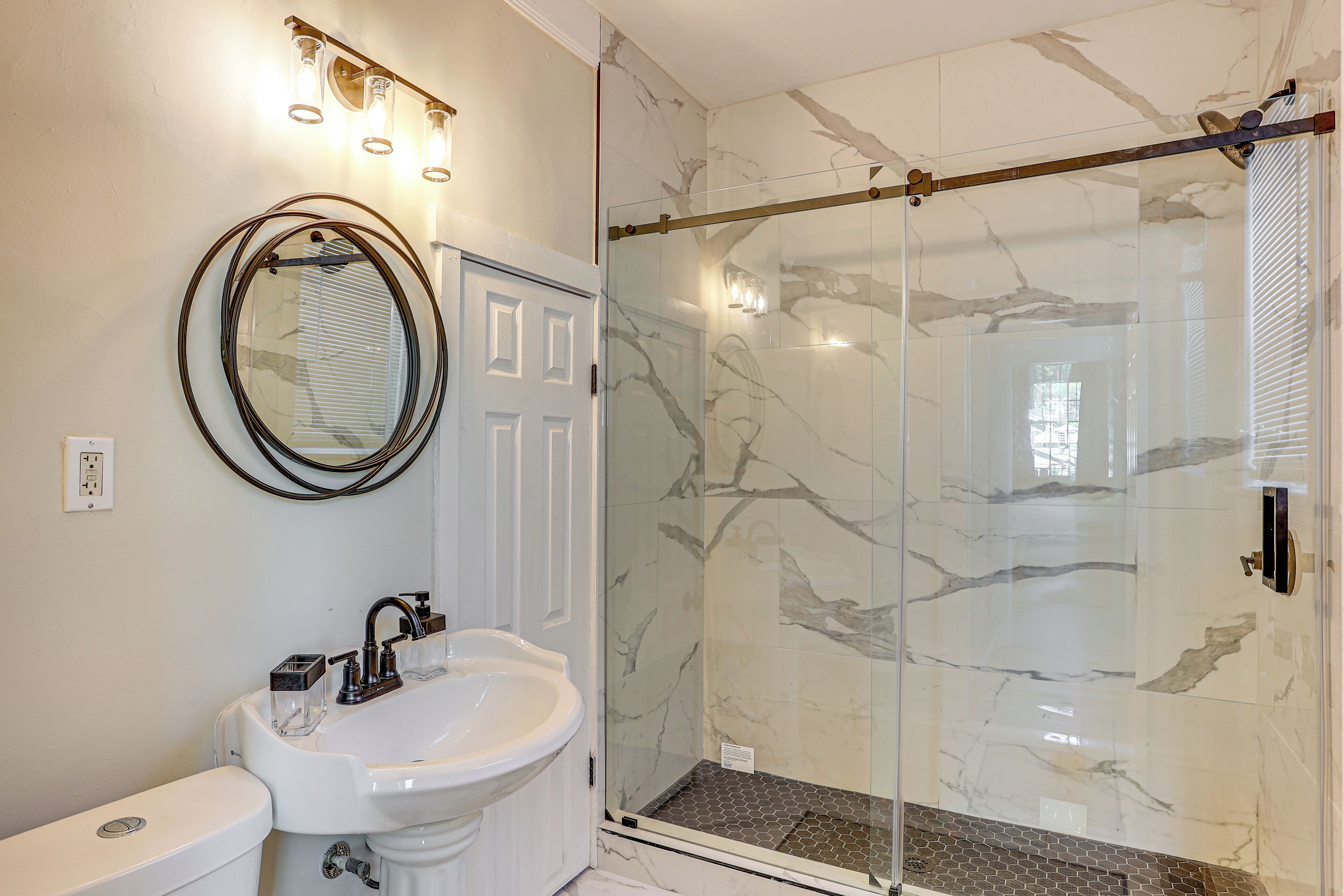 A bathroom with a white sink, a mirror, and a glass shower enclosure with marble tiles.