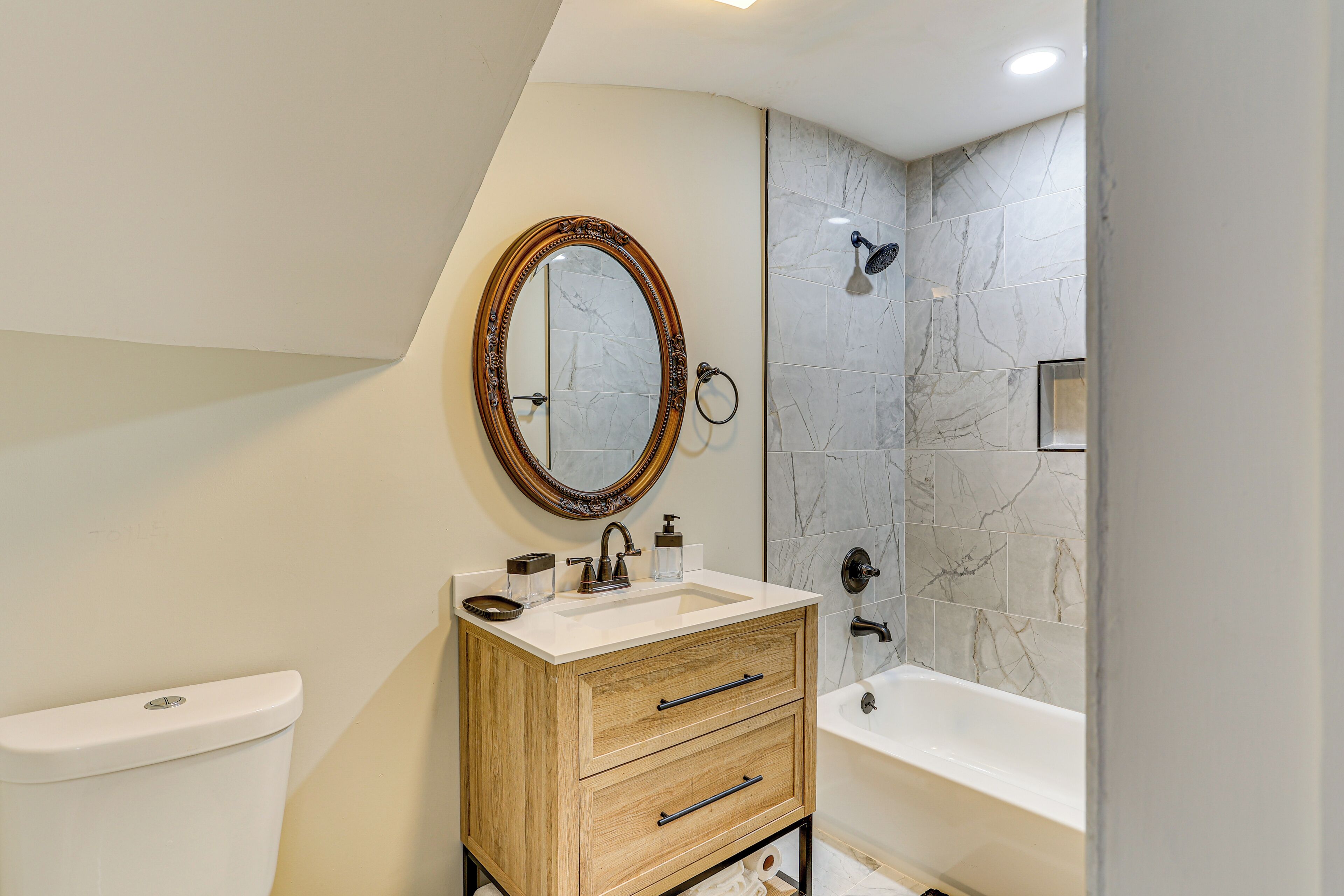 A modern bathroom with a toilet, vanity with drawers, a mirror, a shower, and a bathtub.