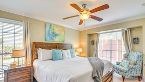 Une chambre avec un grand lit, une tête de lit en bois, un ventilateur de plafond et une vue sur l’extérieur par la fenêtre.