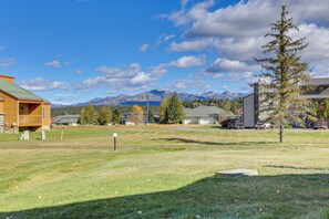 A residential area with a grassy field, a wooden house, and mountains in the background.
