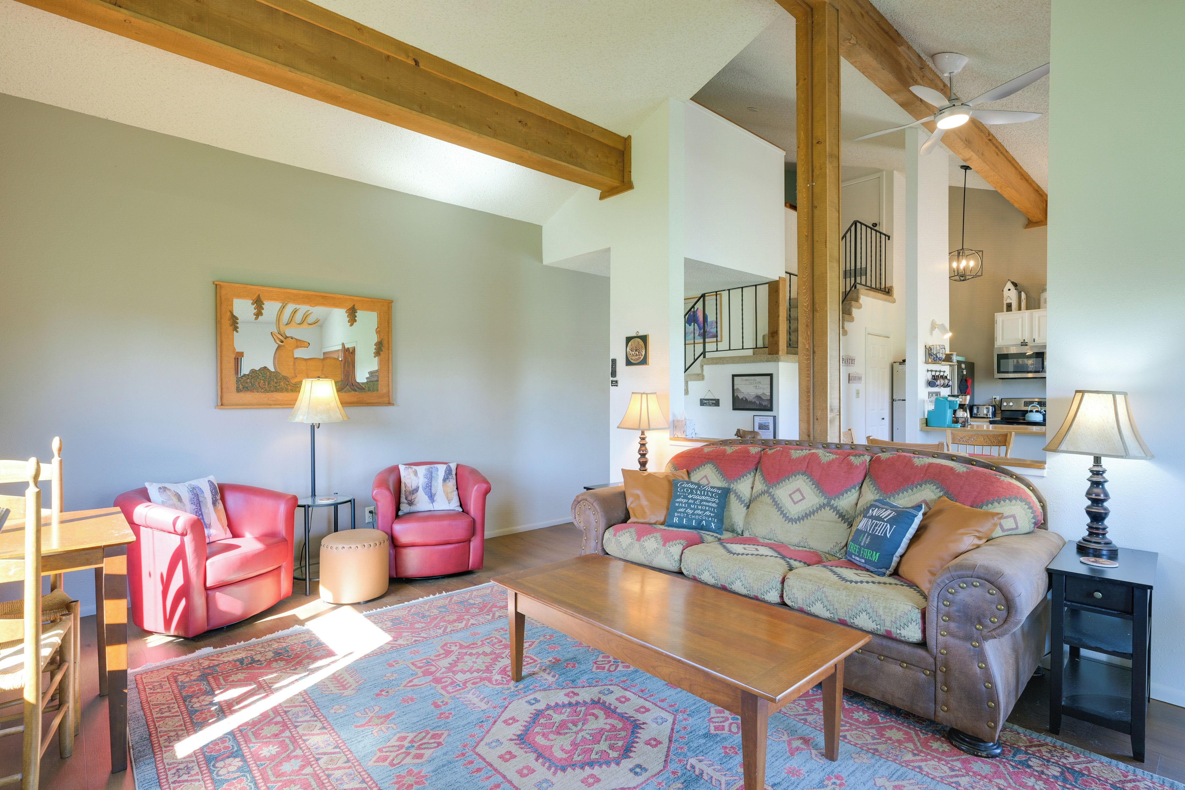 A cozy living room with a wooden coffee table, two red armchairs, a patterned rug, and a large wall painting.