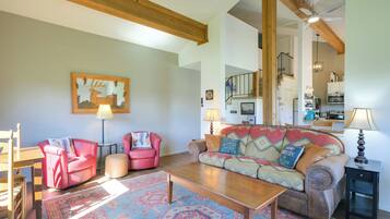 A cozy living room with a wooden coffee table, two red armchairs, a patterned rug, and a large wall painting.