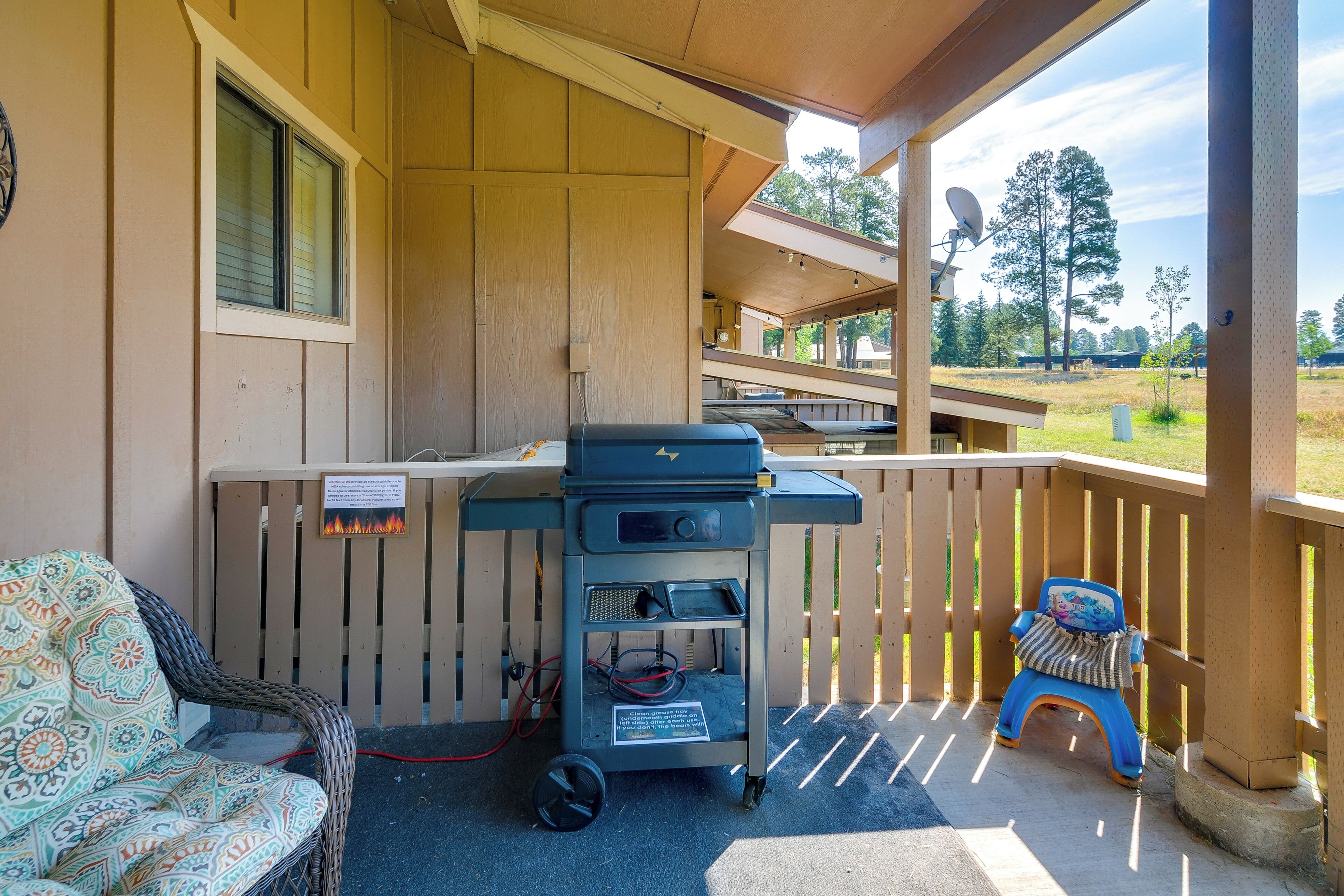 A covered outdoor area with a barbecue grill, a wicker chair, and a small stool.