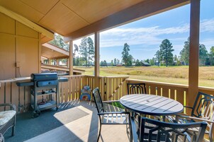 A covered outdoor area with a grill, seating, and a view of a grassy field and trees.