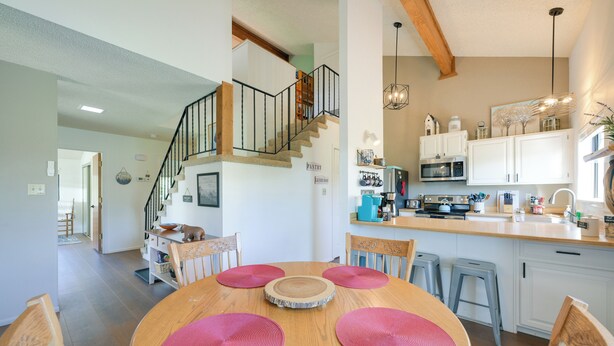 A dining area with a wooden table and chairs, a staircase leading to an upper level, and a kitchen with white cabinets and a microwave. - Uptown Abode 4 Mi to Dtwn Pagosa Springs (Pagosa Springs)