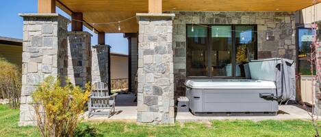 A stone exterior with a hot tub, a covered patio, and a view of the backyard.