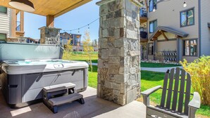 Un jacuzzi bajo una pérgola de madera, un pilar de piedra y una terraza de madera con un banco.