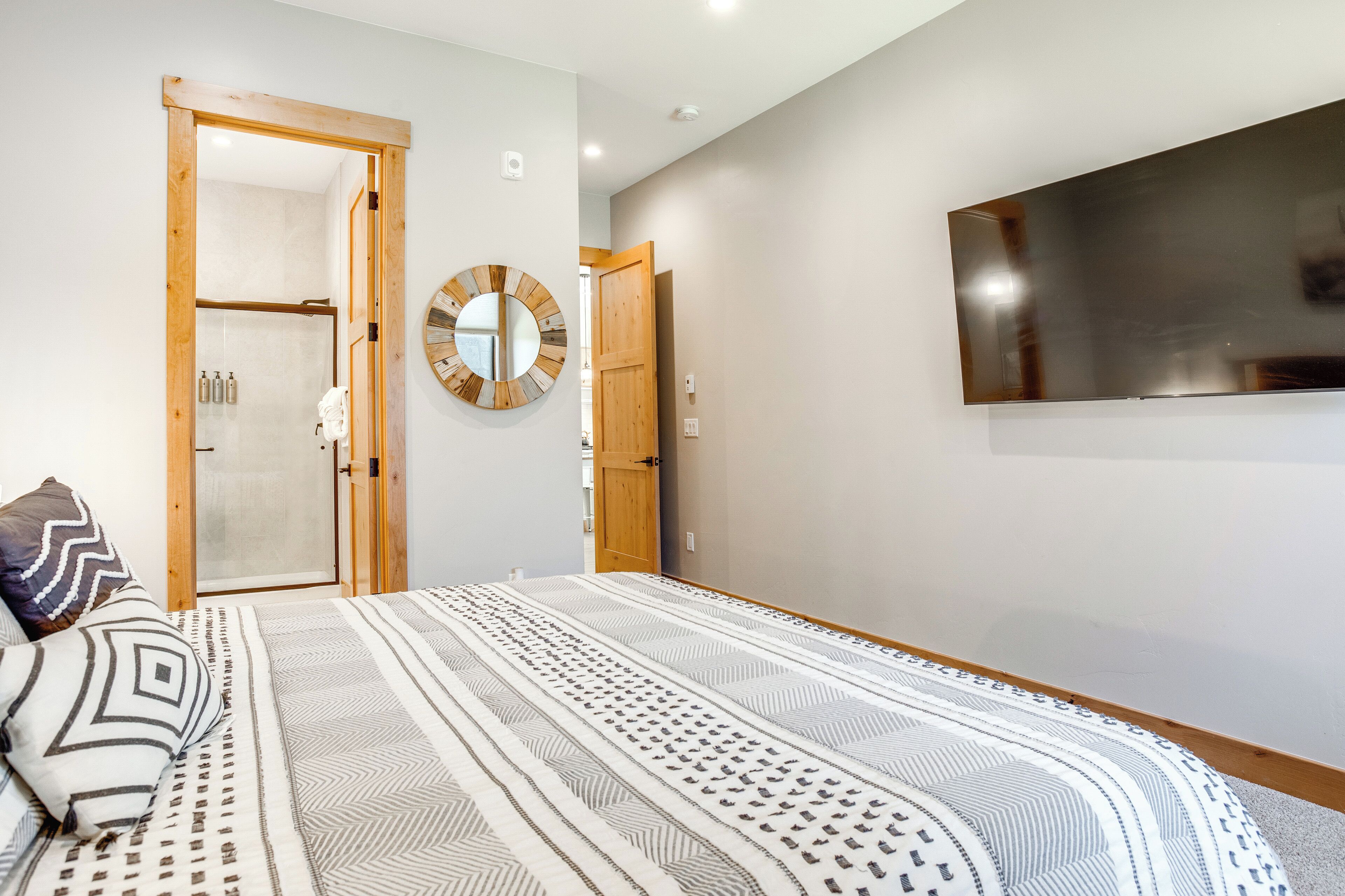 A bedroom with a large bed, a round mirror, and a TV on the wall.