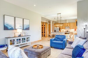 Una sala de estar moderna con un sofá azul, un reposapiés gris y un aparador blanco con puertas de vidrio.