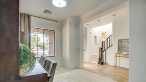 A spacious living area with a dining table, chairs, a staircase, and a view through a large window. - Relax Poolside! Home 6 Mi to Camelback Ranch (Litchfield Park)