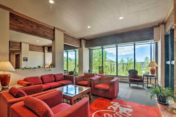 A spacious living area with red upholstered furniture, large windows offering a view of the outdoors, and a modern ceiling design. - Ski-in/ski-out Brian Head Studio (Brian Head)