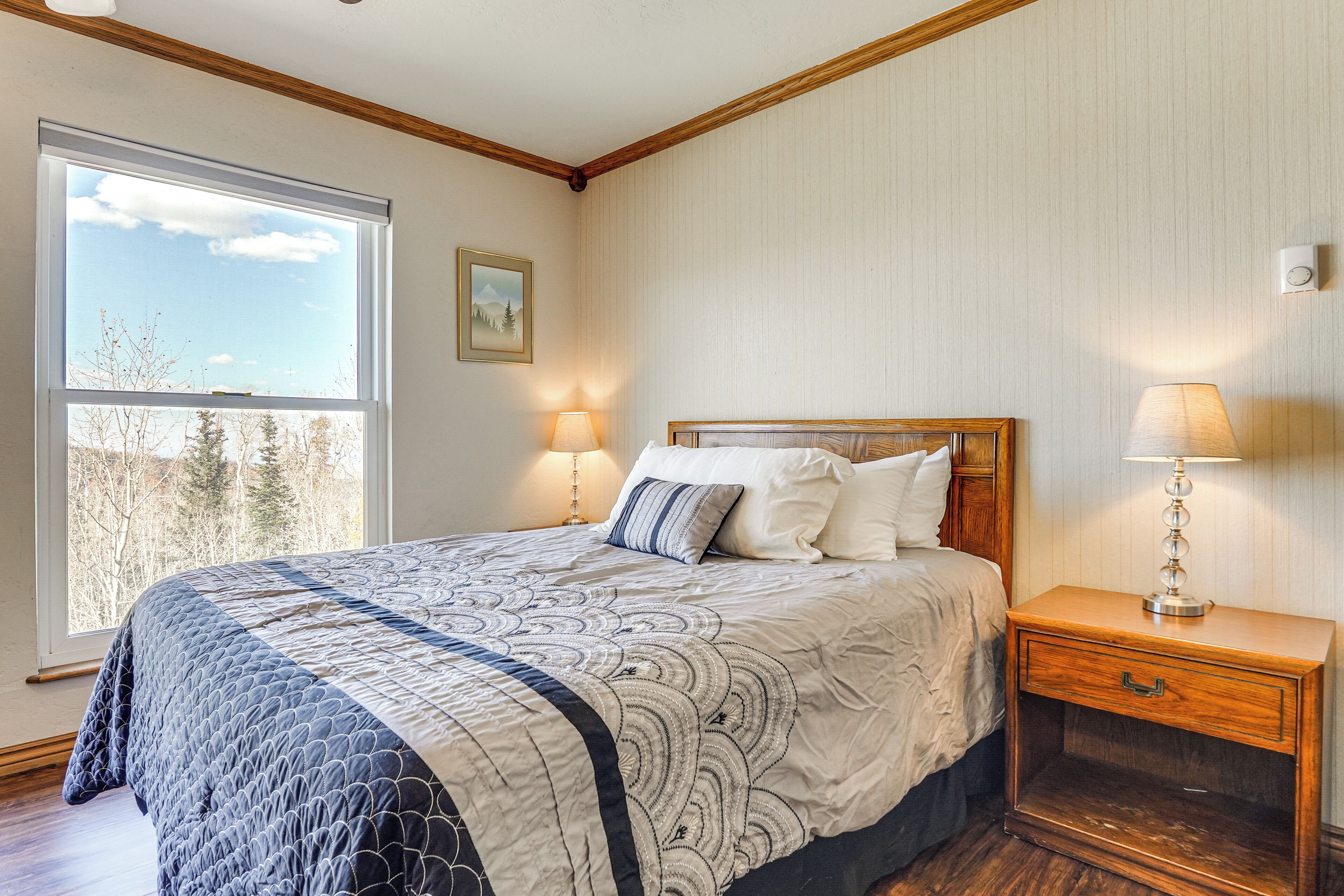 A bedroom with a large window, a bed with a quilt, two bedside lamps, and a nightstand.