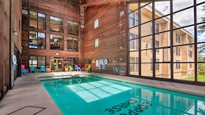 Une piscine intérieure avec un revêtement intérieur en bois, des parois en verre transparent et une vue sur le bâtiment extérieur.