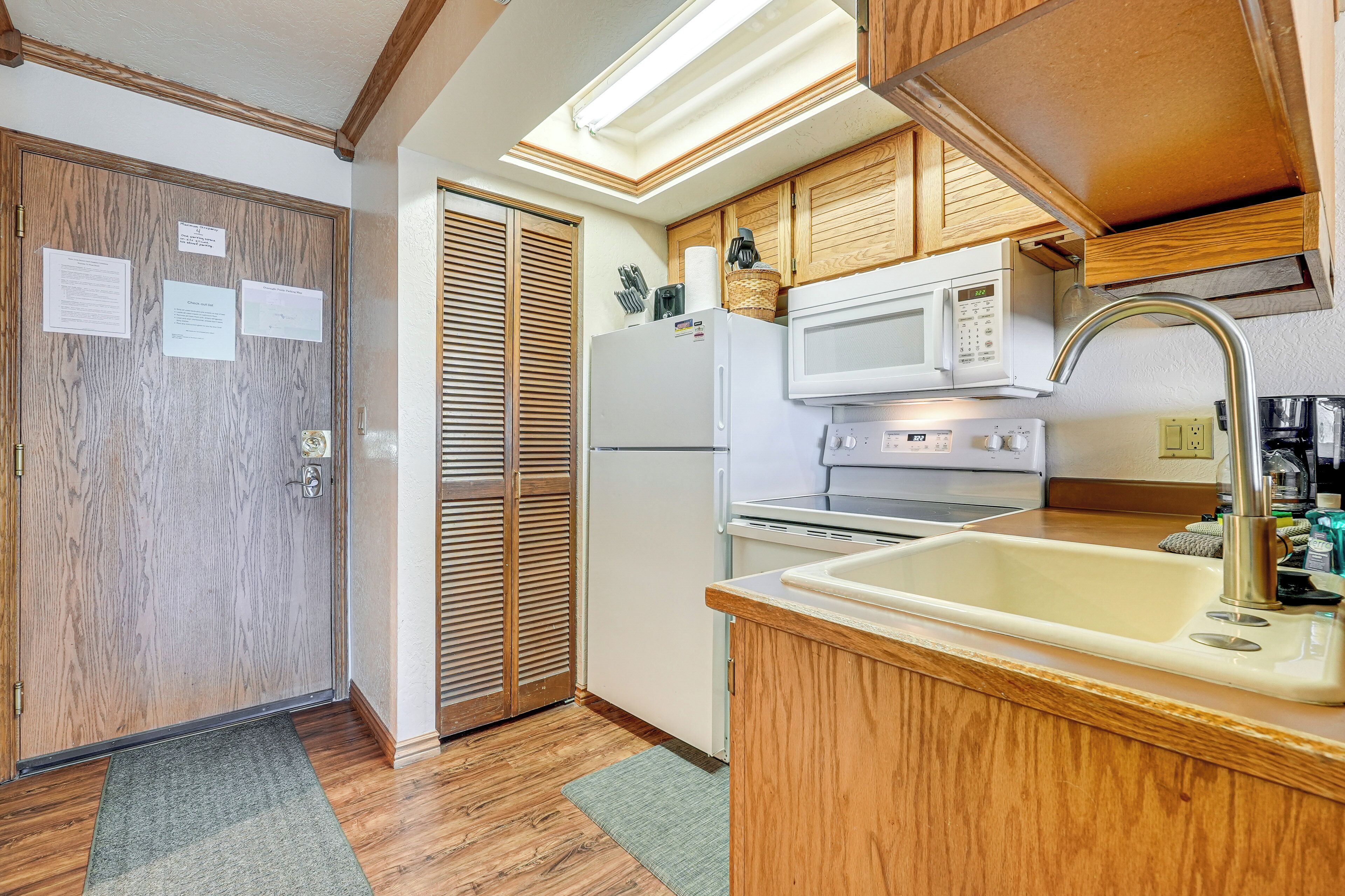 A compact kitchen with wooden cabinets, a built-in microwave, a refrigerator, and a sink.