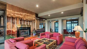 A spacious lobby with red upholstered seating, a glass coffee table, and a fireplace.