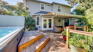 Une maison dotée d’une terrasse en bois, d’un jacuzzi et d’un patio couvert.