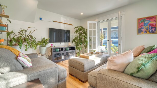 A modern living room with grey sofas, a flat-screen TV, a large potted plant, and a sliding glass door leading to a balcony.