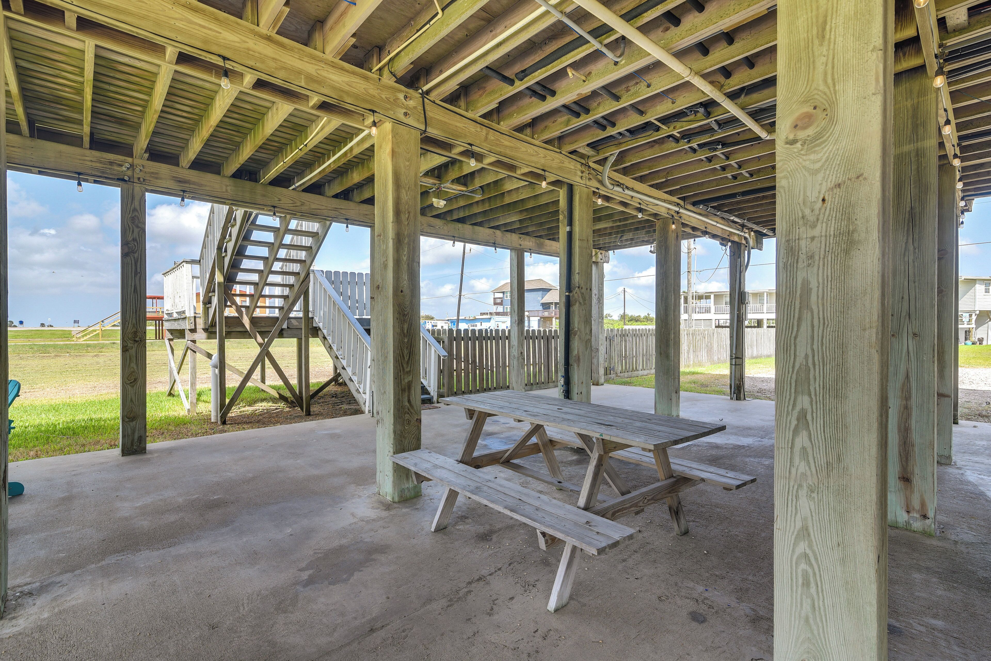 A wooden picnic table under a covered area with a concrete floor, surrounded by wooden beams and columns.