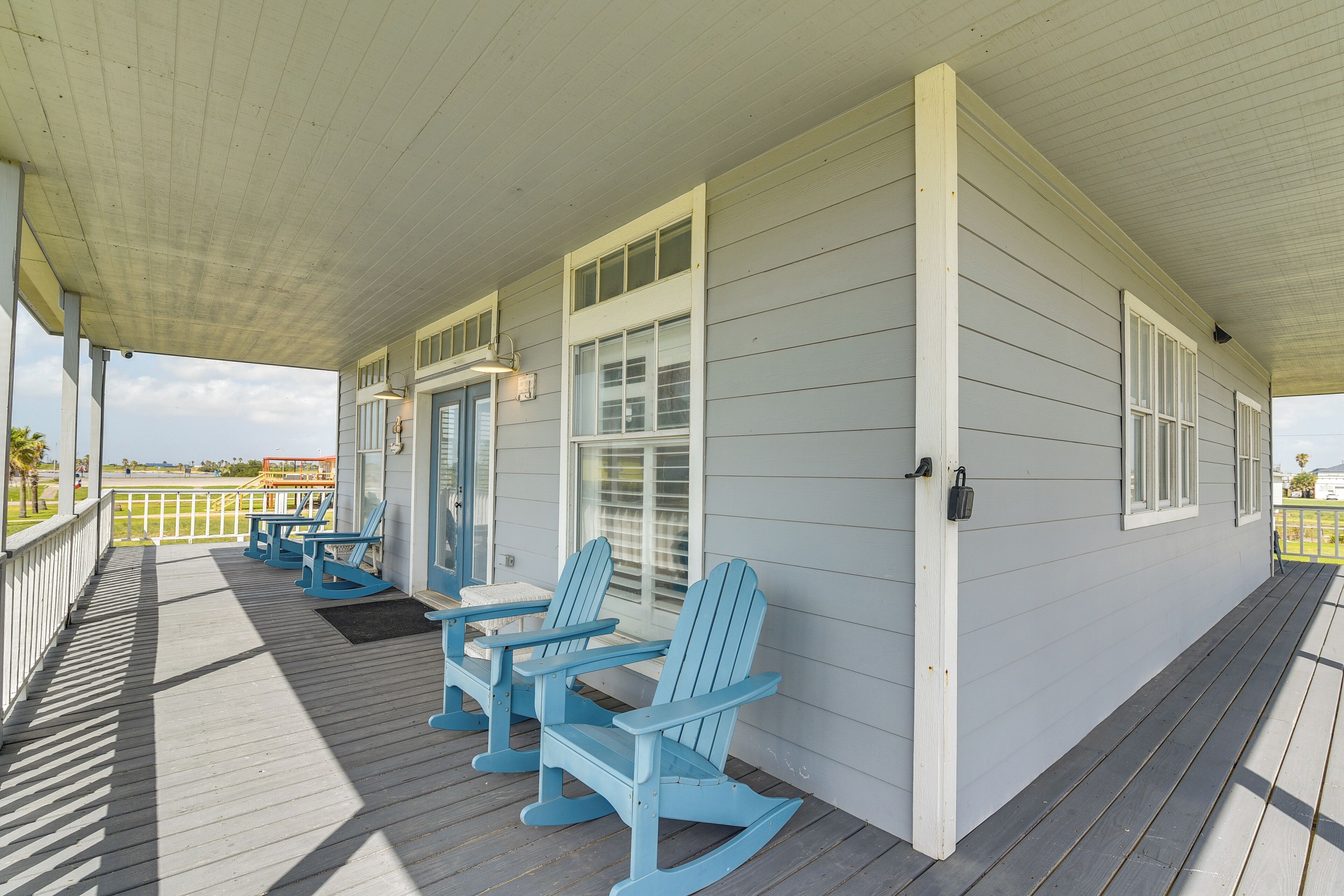 Une véranda couverte avec des fauteuils Adirondack bleus et une balustrade blanche.