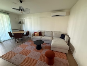 A modern living room with a sofa, a dining table with chairs, a small round table, and a ceiling fan. - Le Piou Vert (Annecy)