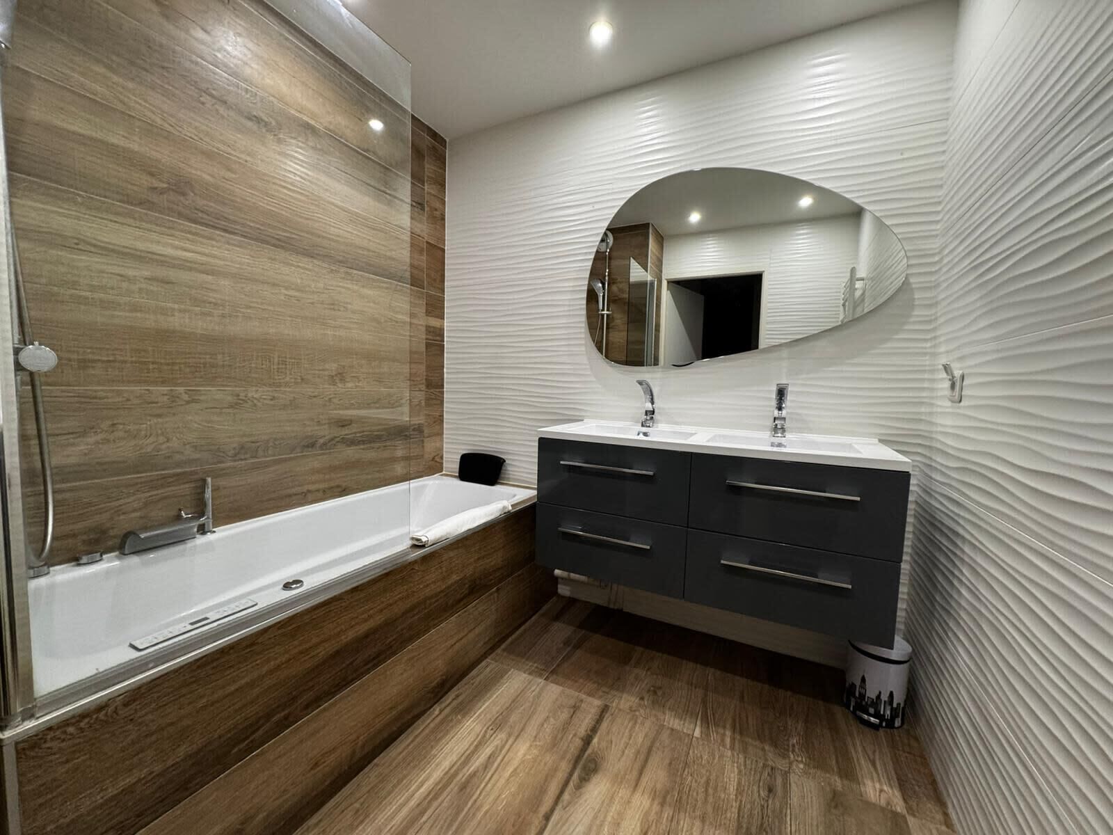 A modern bathroom with a wooden vanity, a large mirror, and a bathtub.
