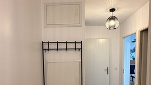 Un couloir avec un présentoir métallique, une porte et un luminaire au plafond.