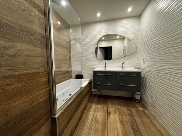 A modern bathroom with a wooden floor, a freestanding bathtub, a vanity with a mirror, and a towel rack.