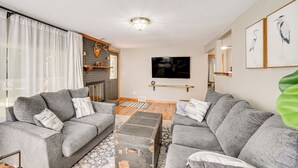 A modern living room with grey sofas, a wooden coffee table, and a flat-screen TV mounted on the wall. - Walk to Water: Lake House in Suring! (Suring)