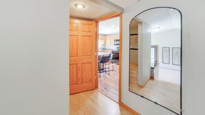 A hallway with wooden flooring, a wooden door, and a mirror reflecting a dining area with chairs and a table. - Walk to Water: Lake House in Suring! (Suring)