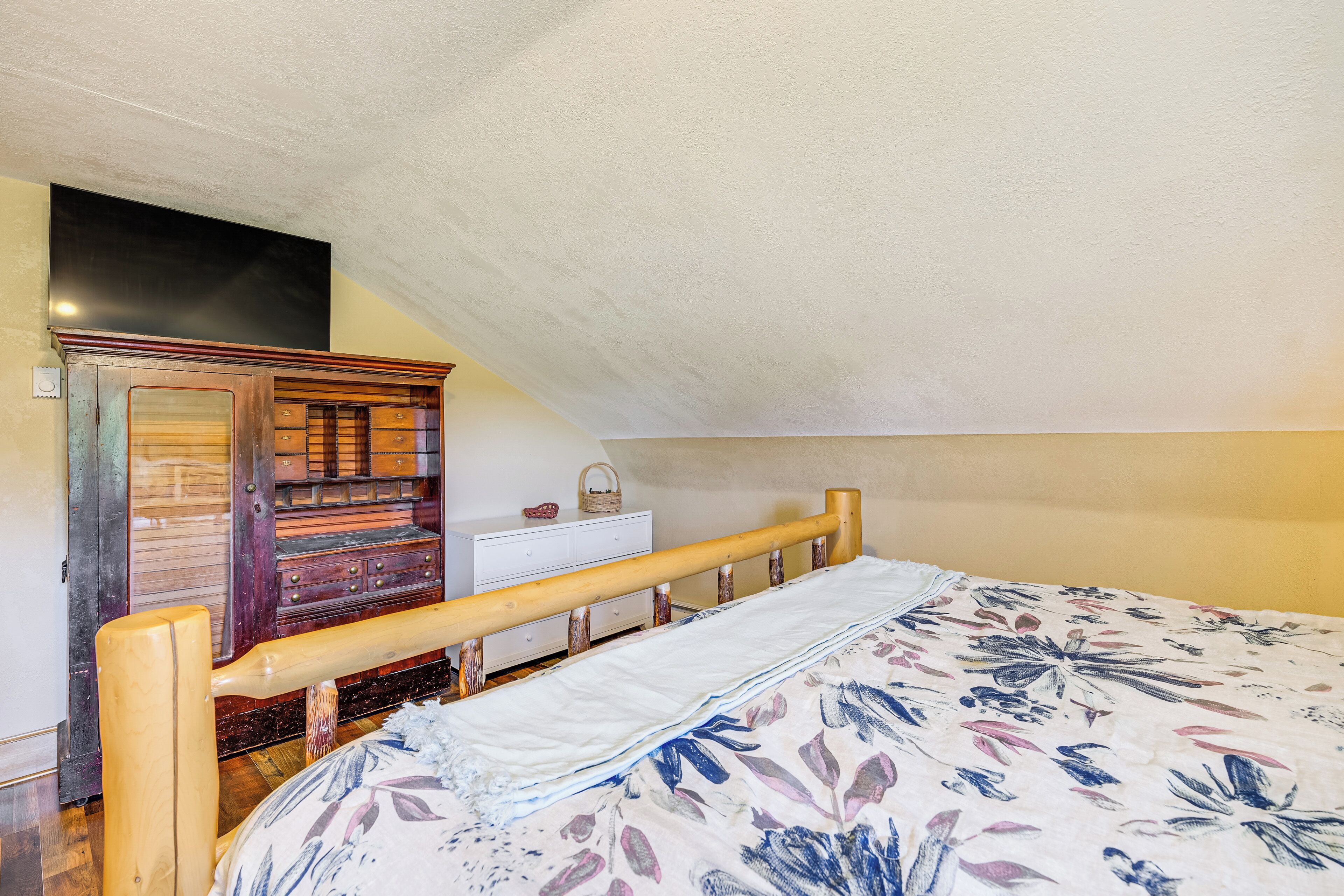 Un dormitorio con cabecero de madera, cómoda blanca y techo inclinado.