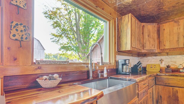 A kitchen with wooden cabinets, a stainless steel sink, and a window with a view of trees. - Pet-friendly Farmhouse Near Lakes in Pellston (Pellston)