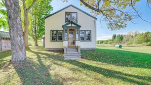 A two-story house with a front porch, a lawn, and trees. - Pet-friendly Farmhouse Near Lakes in Pellston (Pellston)