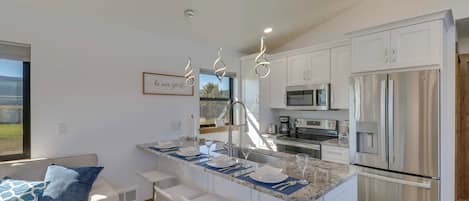 A modern kitchen with white cabinetry, stainless steel appliances, and a central island with bar stools.