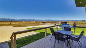 Een terras met tafel en stoelen, met uitzicht op een grasveld en bergen.