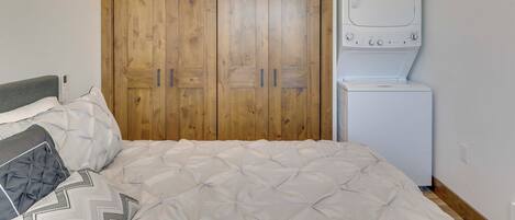 Un dormitorio con un armario de madera, lavadora y una cama con ropa de cama estampada.