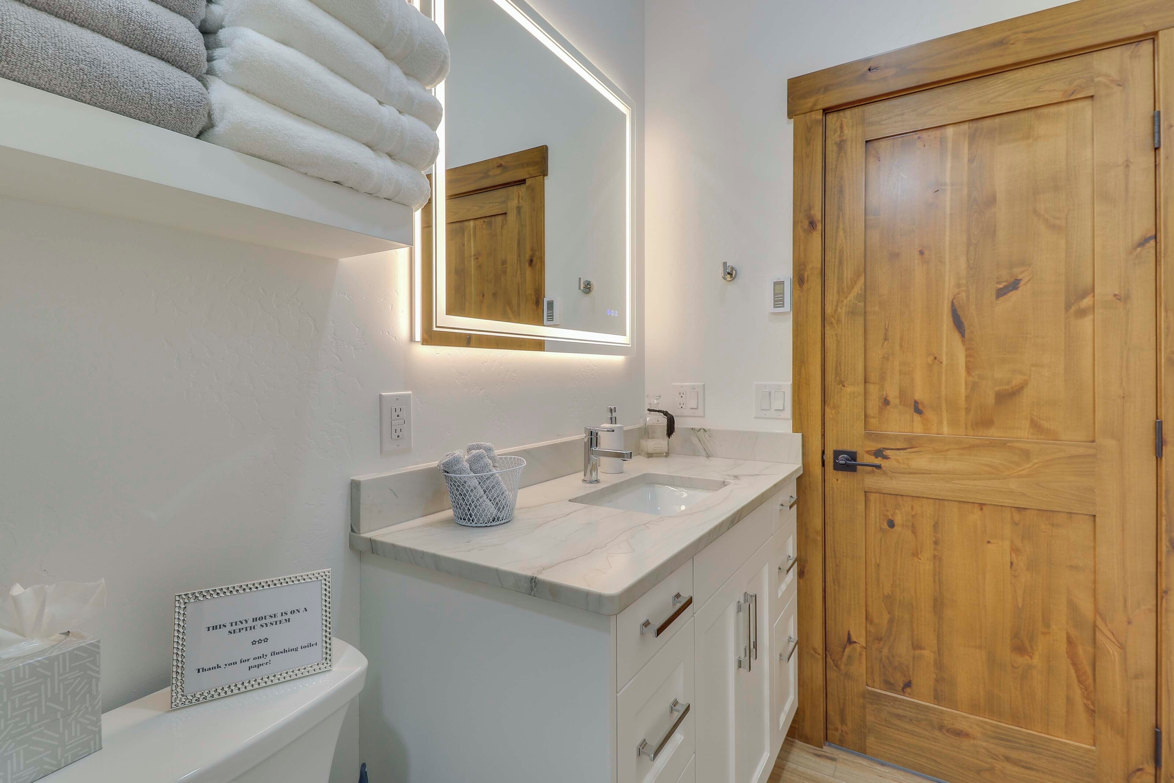 Un baño con puerta de madera, un lavabo blanco y un espejo con marco de madera.