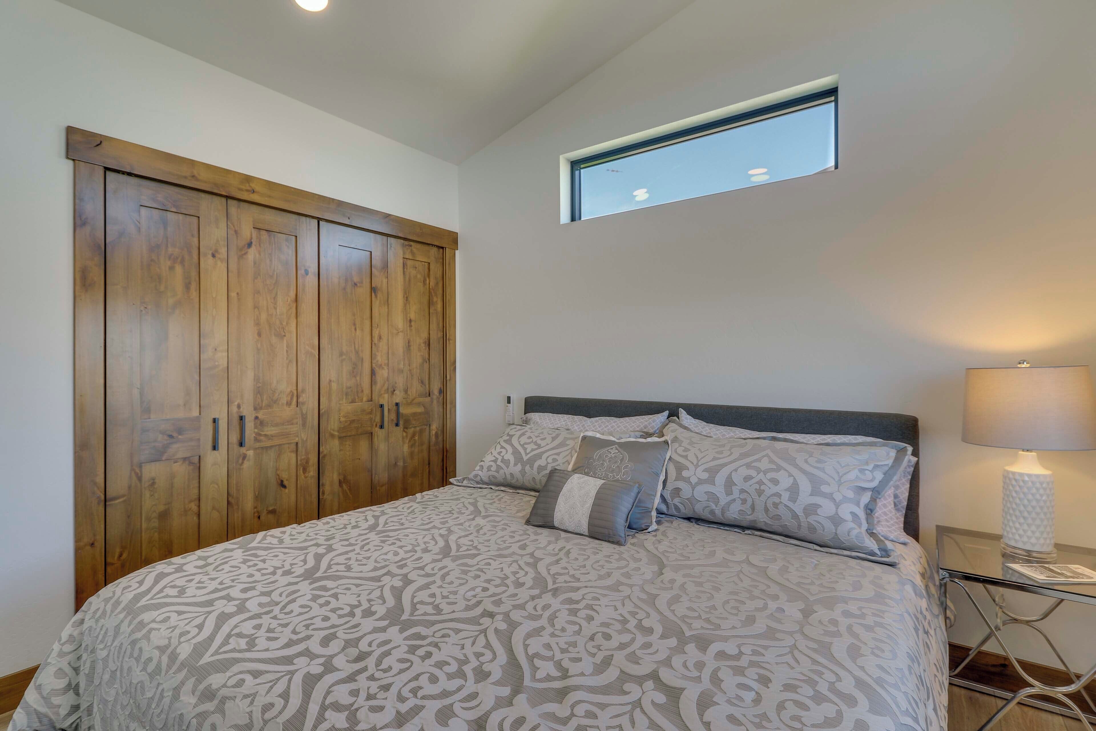 Une chambre à coucher avec un grand lit, une armoire en bois, une petite fenêtre et une table de chevet avec une lampe.