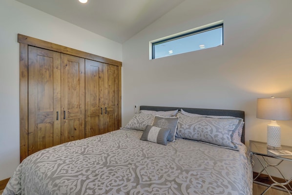 A bedroom with a large bed, a wooden wardrobe, a small window, and a bedside table with a lamp.