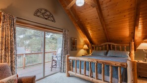 A cozy bedroom with a wooden bed, a large window with curtains, a small table, and a chair. - Cozy Cabin | New Hot Tub! Near Shopping, Dining, Skiing, Golfing (Pagosa Springs)