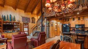 A spacious living area with a wooden ceiling, a fireplace, a dining table, and a kitchen with modern appliances. - Cozy Cabin | New Hot Tub! Near Shopping, Dining, Skiing, Golfing (Pagosa Springs)