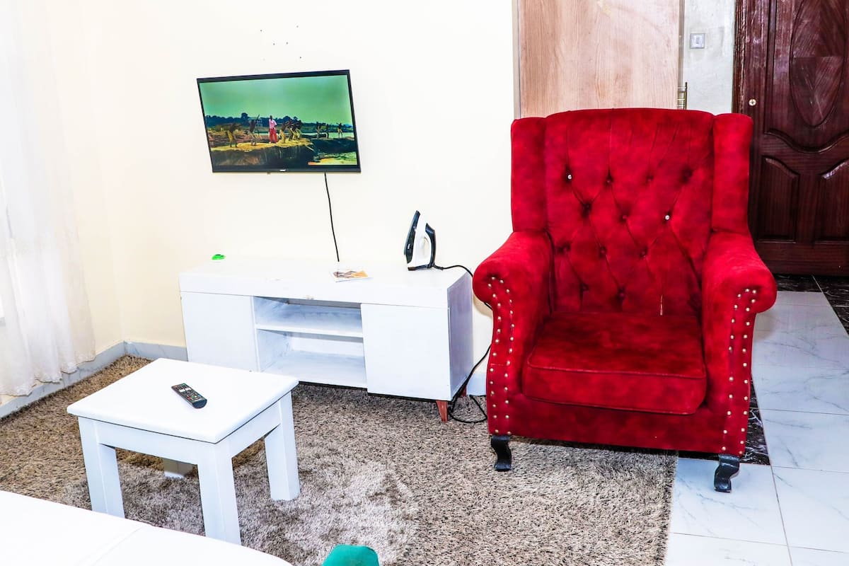 A living room with a red armchair, a white TV stand, a remote control on a small table, and a picture on the wall.