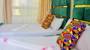 A hotel room with two beds, each with colorful patterned pillows, a green upholstered headboard, and a white bedspread. - Lux Suites Kwamby Ocean paradise (Mombasa)