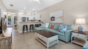 A spacious living room with a light blue sofa, a wooden coffee table, and a kitchen in the background. - Modern 2BR/2BA Condo Near Beach + Free Attraction Tickets! (Santa Rosa Beach)