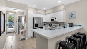 A modern kitchen with white cabinetry, stainless steel appliances, and a central island with bar stools. - Modern 2BR/2BA Condo Near Beach + Free Attraction Tickets! (Santa Rosa Beach)