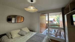 Een slaapkamer met een bed, een hanglamp, een spiegel en een glazen schuifdeur naar een buitenruimte met een houten terras en stoelen.